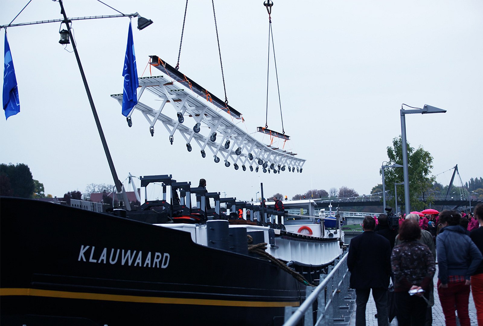 Close-up of a steel beam suspended by a chain above the long white marina tabletop, with orange straps stretched across the surface.