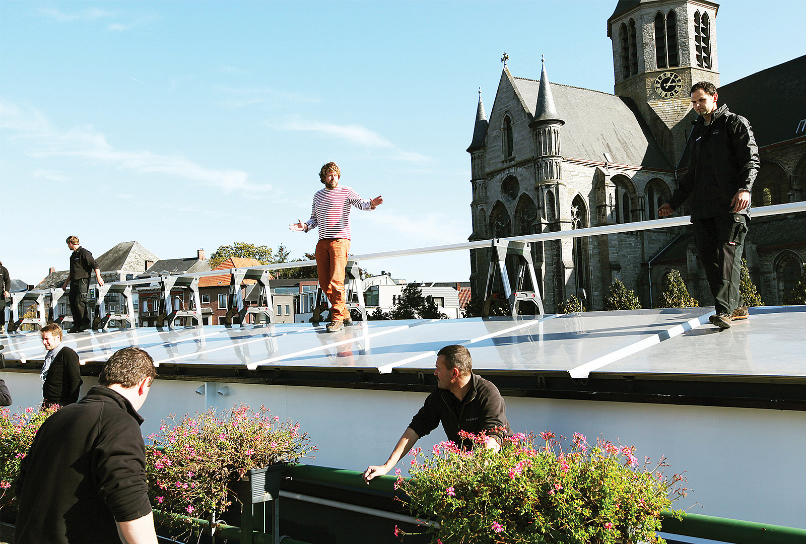 Dirk handling a long white beam across sawhorses on the roof of the cargo boat beside the canal.