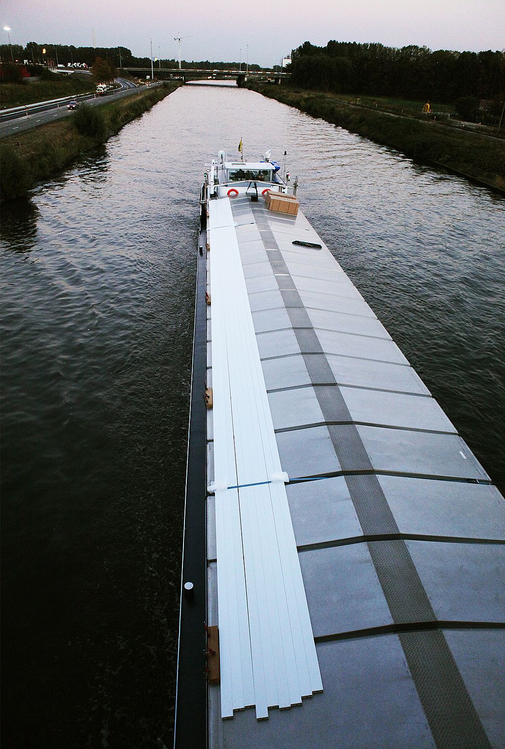 Une très longue section de table blanche attachée le long du pont d’un cargo naviguant sur un canal, vue d’en haut.