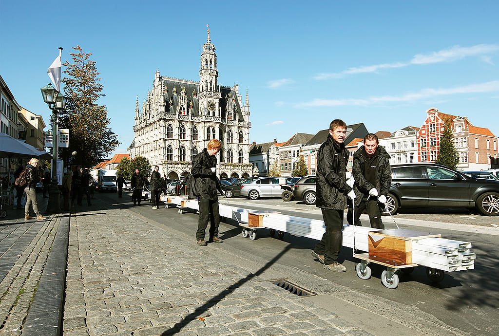 Des ouvriers se tiennent au sommet d’un cargo près d’une église, préparant de longs éléments de table blancs pour le déchargement.