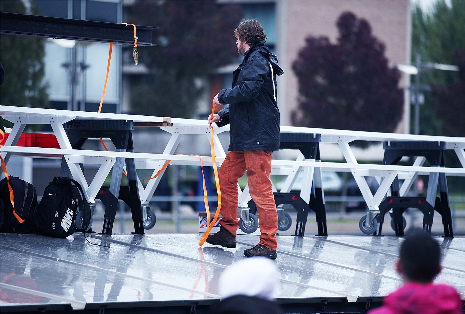 Dirk securing a long white Marina table section with orange straps on a wet platform during setup.