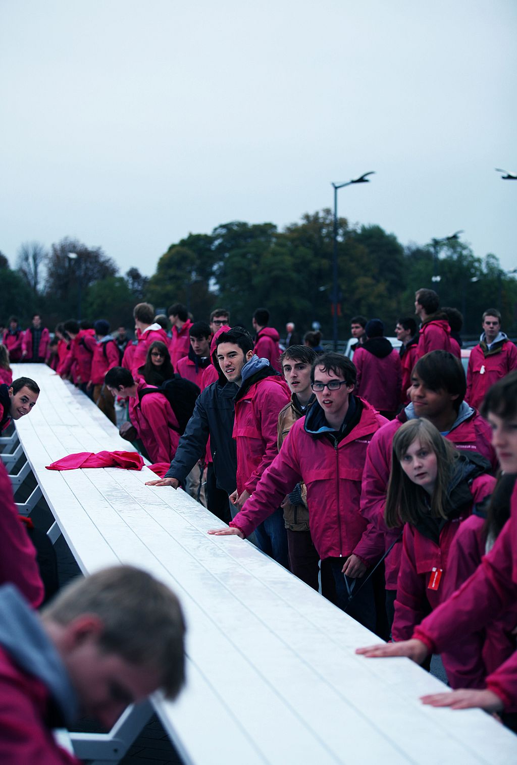 Des gens poussent ou guident la longue table blanche à travers une grande salle d’exposition avec des poutres en bois voûtées au-dessus.