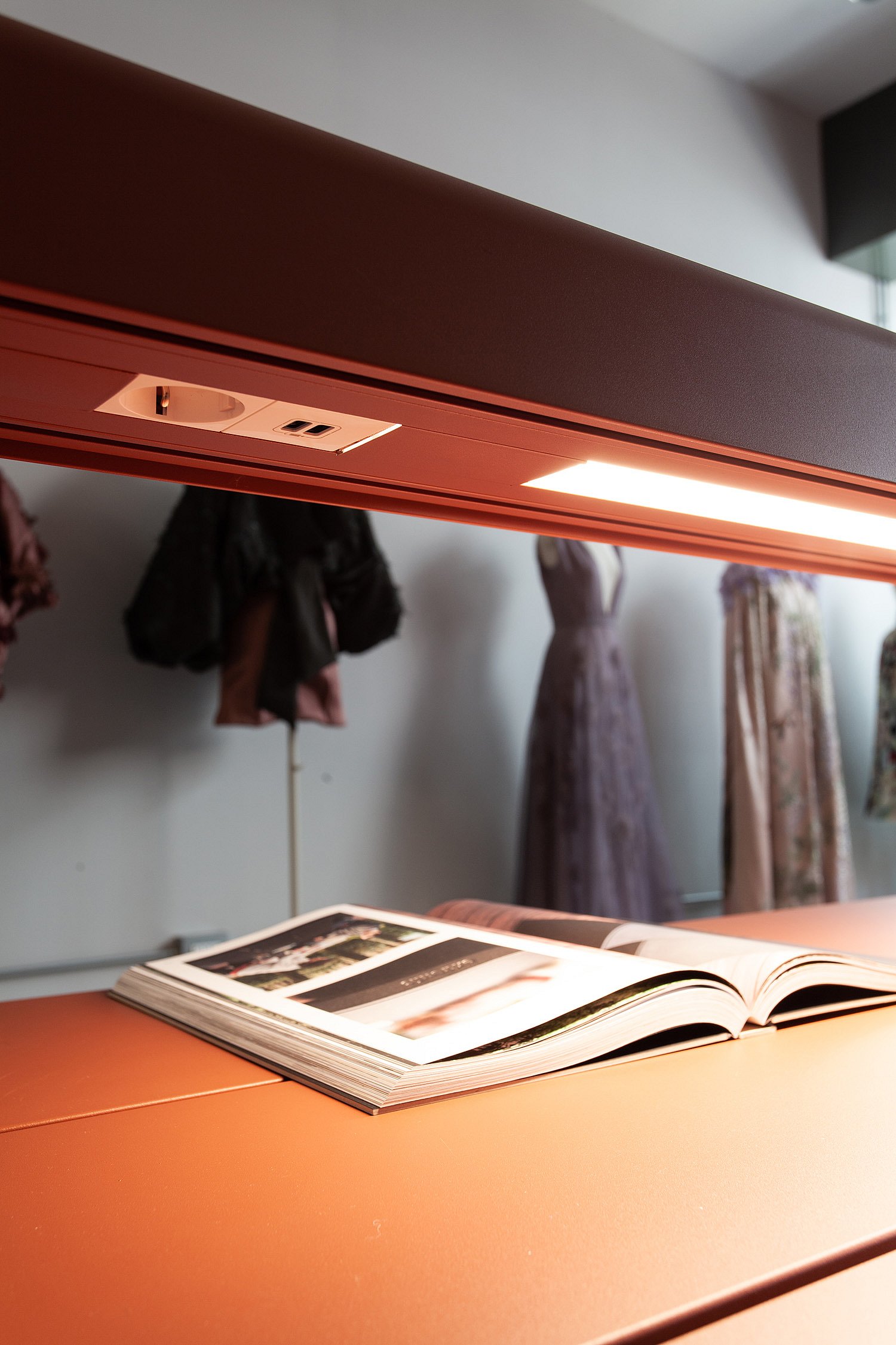 Gros plan sur une structure de table suspendue couleur rouille avec éclairage intégré et prises électriques, au-dessus d'un livre ouvert posé sur le plateau.