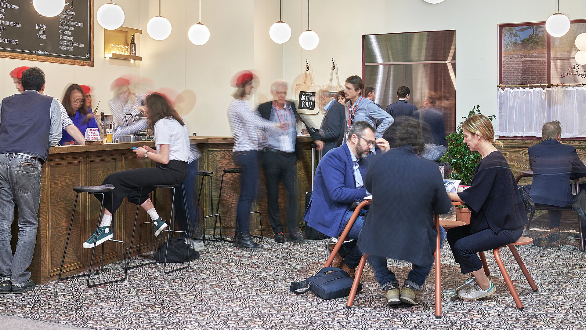 Scène de comptoir avec plusieurs tabourets de bar slim noirs Tiki alignés devant, tandis que les visiteurs discutent avec le personnel derrière le comptoir.