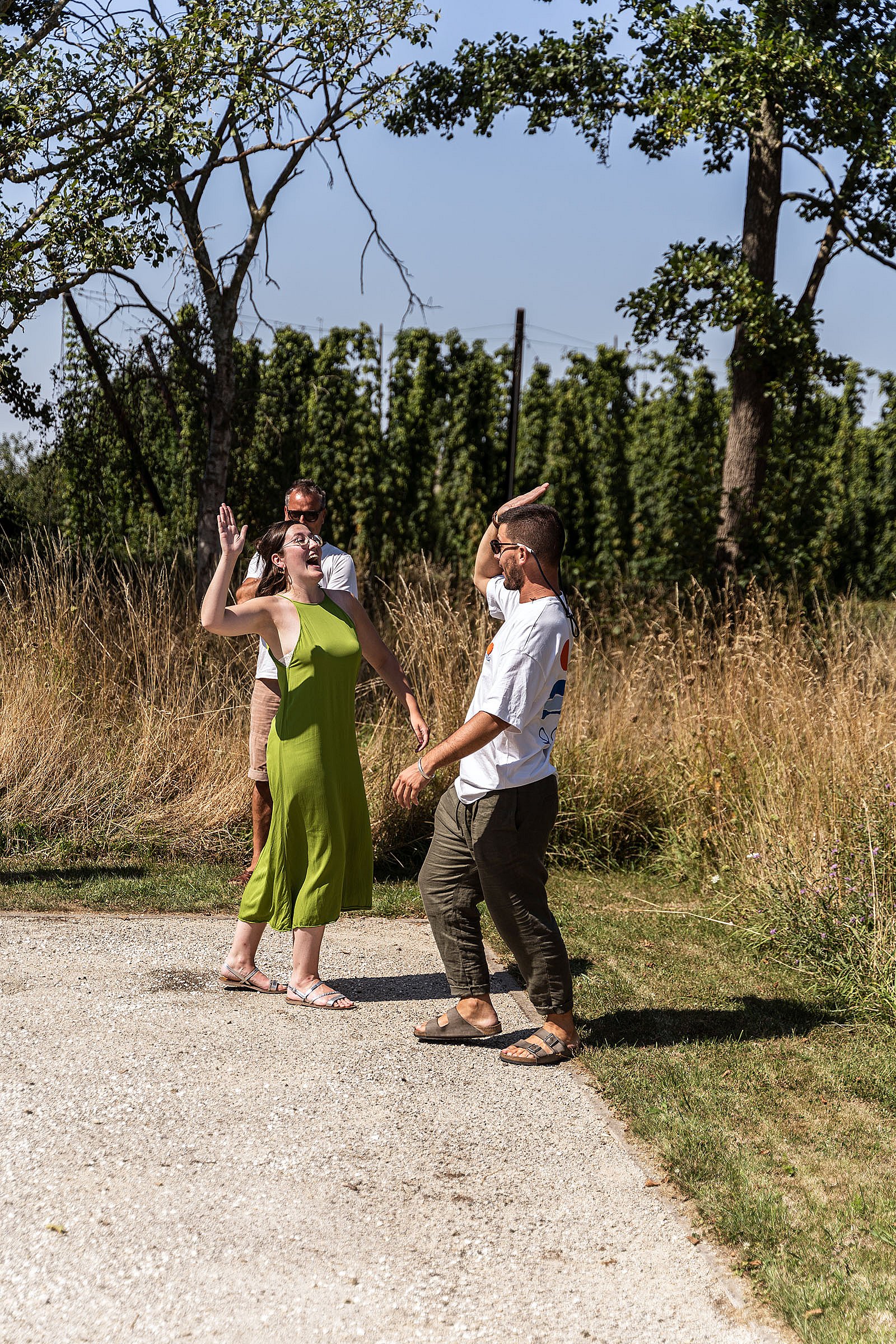 Zwei Teamkollegen feiern auf dem Pétanque-Platz mit erhobenen Händen und stehen vor trockenem Gras und Bäumen.