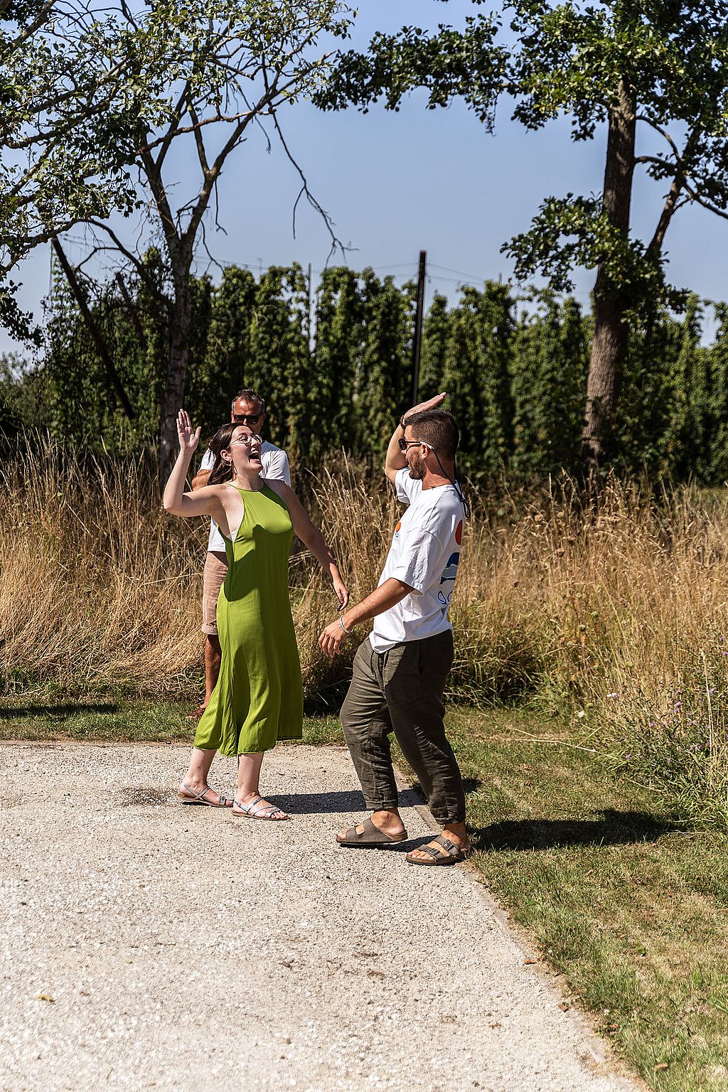 Zwei Teamkollegen feiern auf dem Pétanque-Platz mit erhobenen Händen und stehen vor trockenem Gras und Bäumen.