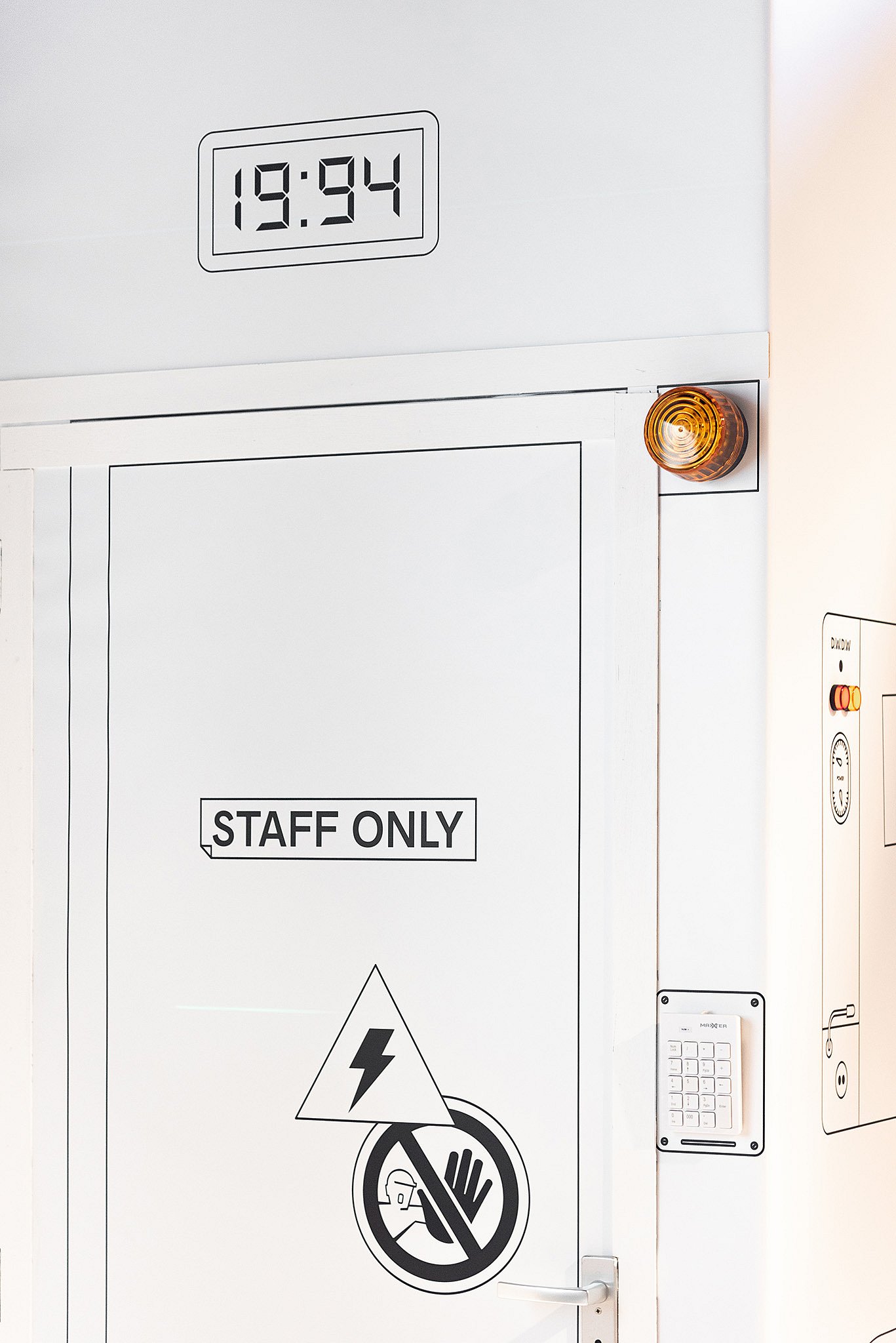Gros plan sur une porte de cabine blanche portant l'inscription « Personnel uniquement ». avec une horloge numérique et un voyant lumineux orange, renforçant l'atmosphère ludique de laboratoire de haute puissance.