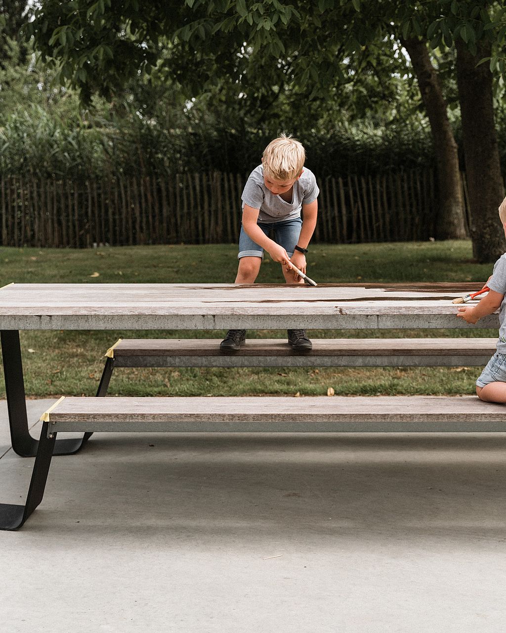 Scène de ménage de printemps en famille autour d’une table en bois à l’extérieur, introduisant le rafraîchissement annuel des meubles de jardin après l’hiver.