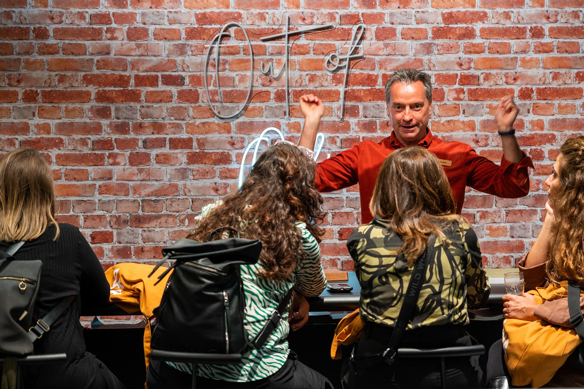 Un homme en chemise rouge montre la teinte horizontale coulissante sur une table AMAi de couleur rouille, tandis que les visiteurs regardent devant un fond extérieur vert.