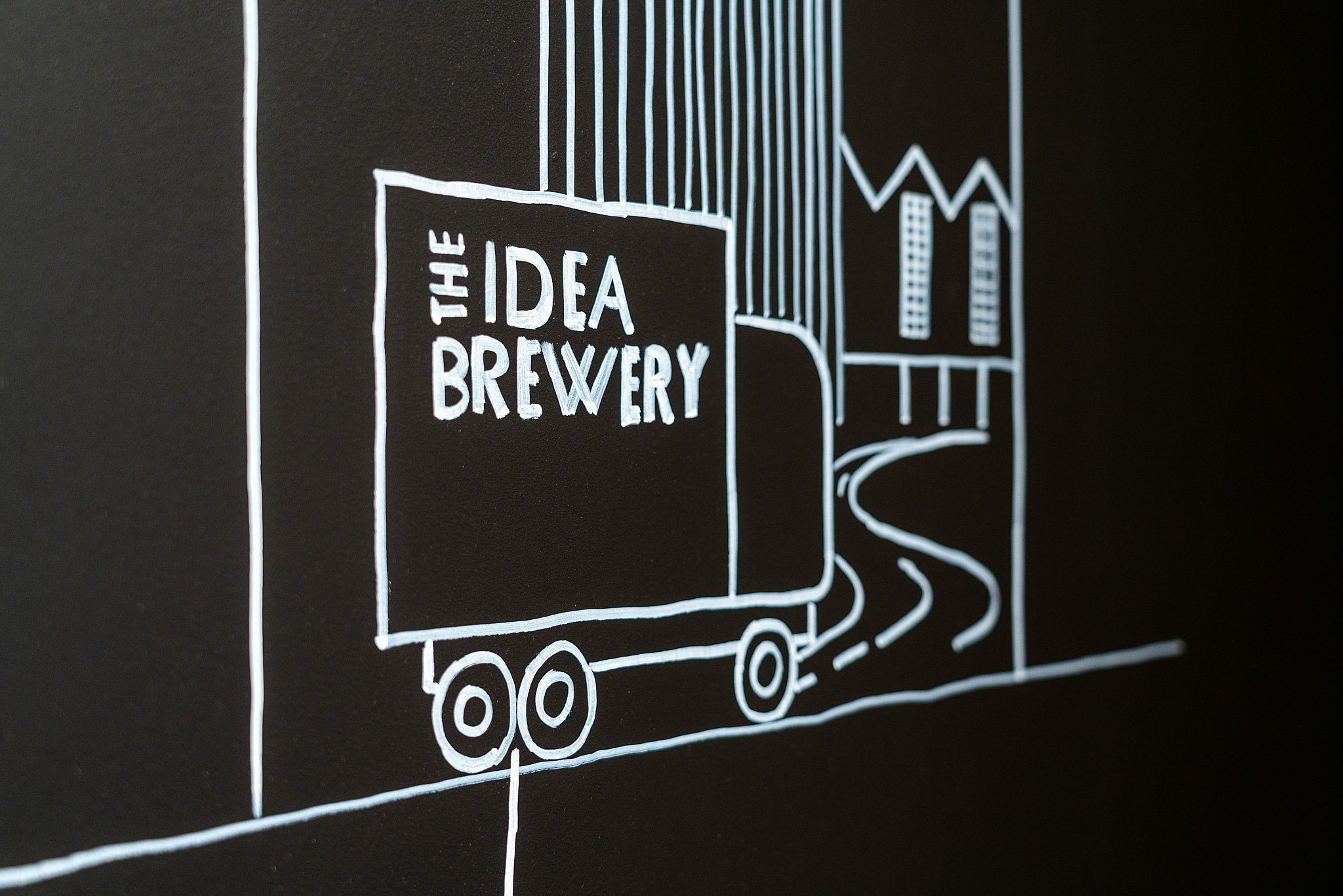 Gros plan d’un dessin mural de style craie représentant un camion de livraison étiqueté « The Idea Brewery », suggérant des idées en cours d’expédition à partir du concept de l’espace de travail.
