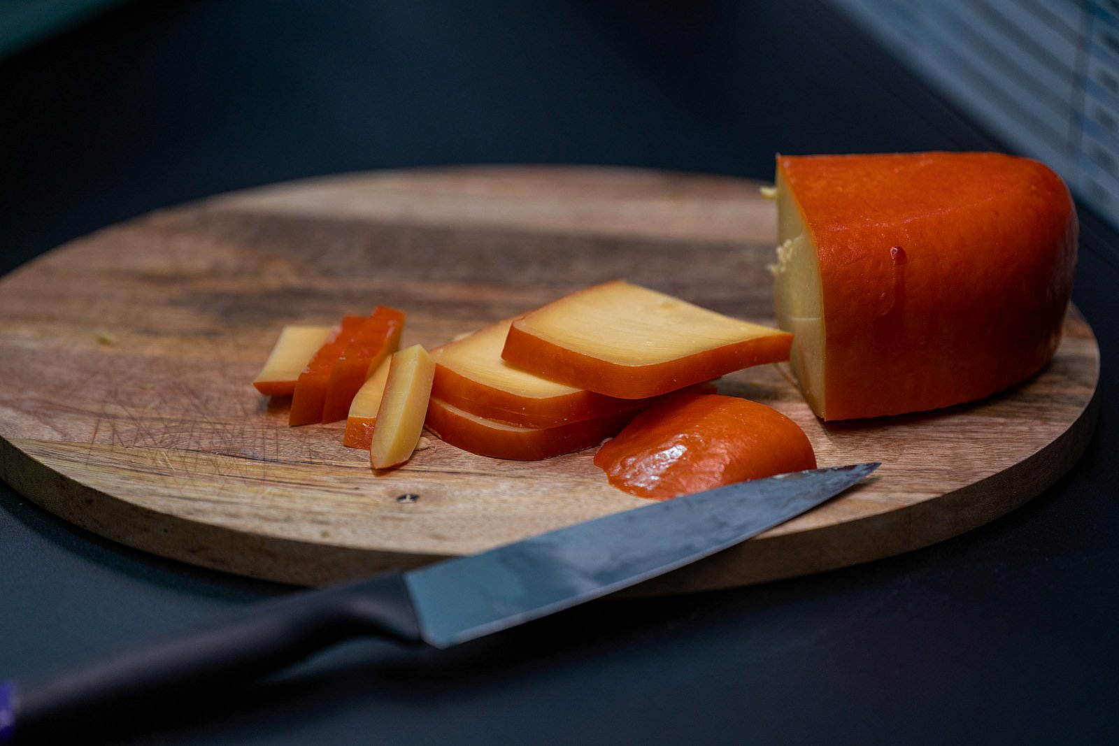 Gros plan sur du fromage à croûte d’orange tranché sur une planche de bois ronde avec un couteau, faisant écho à l’ambiance brasserie-bar du stand.