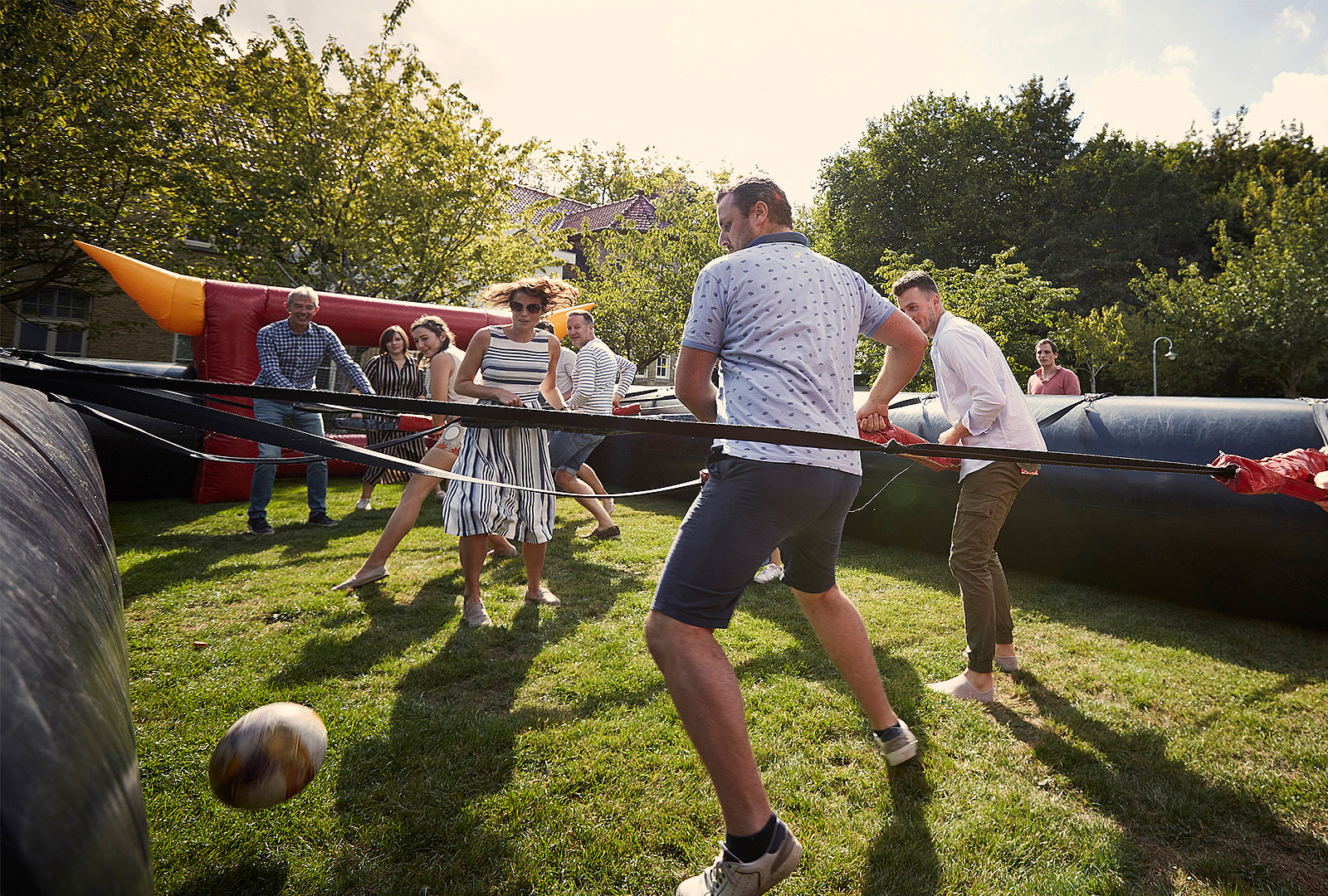  Eine Gruppe Erwachsener spielt Menschenkicker auf dem Rasen in einem aufblasbaren Freiluft-Spielfeld.