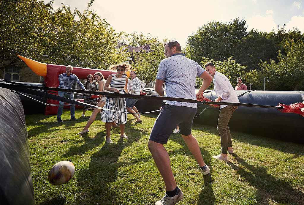 Eine Gruppe Erwachsener spielt Menschenkicker auf dem Rasen in einem aufblasbaren Freiluft-Spielfeld.