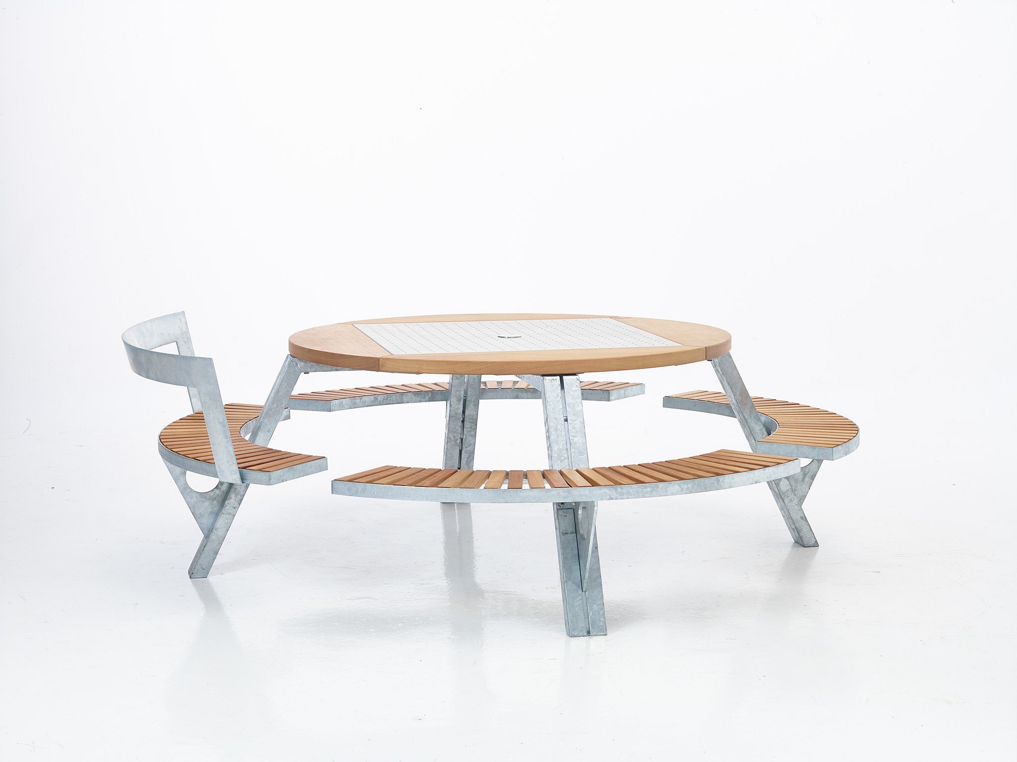 Close-up of a round wooden outdoor table with curved slatted seating and a perforated metal insert in the center.