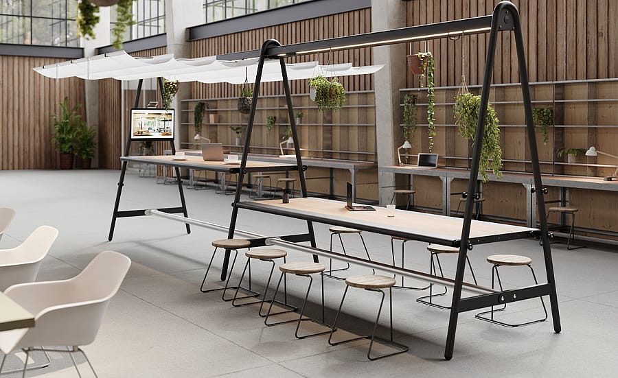 Moderne binnenwerkruimte met twee lange AMAi-tafels, krukken, hangende planten en geïntegreerde bovenliggende schaduwstructuren in een licht kantoor in industriële stijl.