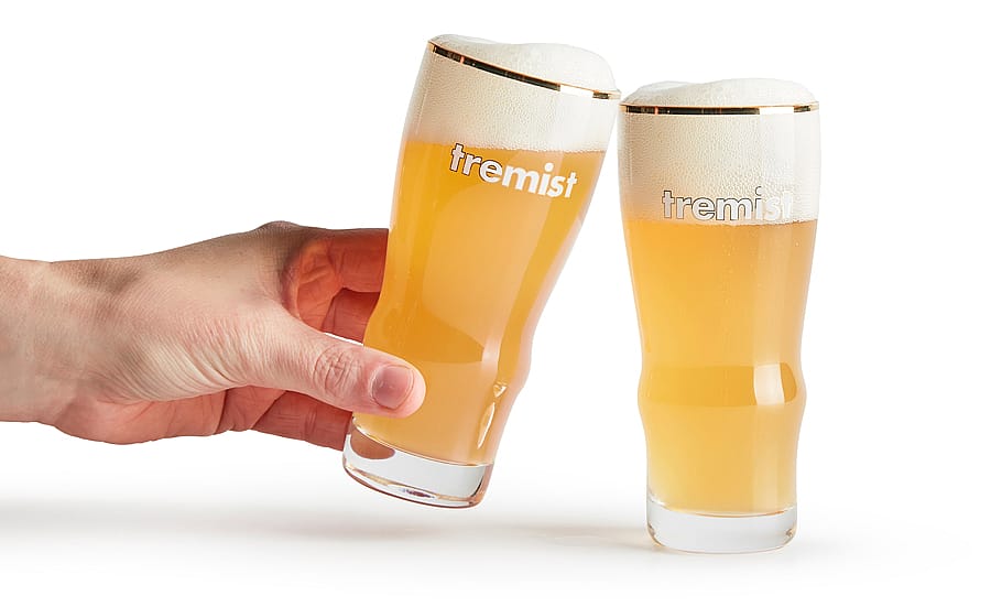 Hand met een glas bleek bier naast een tweede vol Tremistisch bierglas met een dikke schuimige kop op een eenvoudige achtergrond.