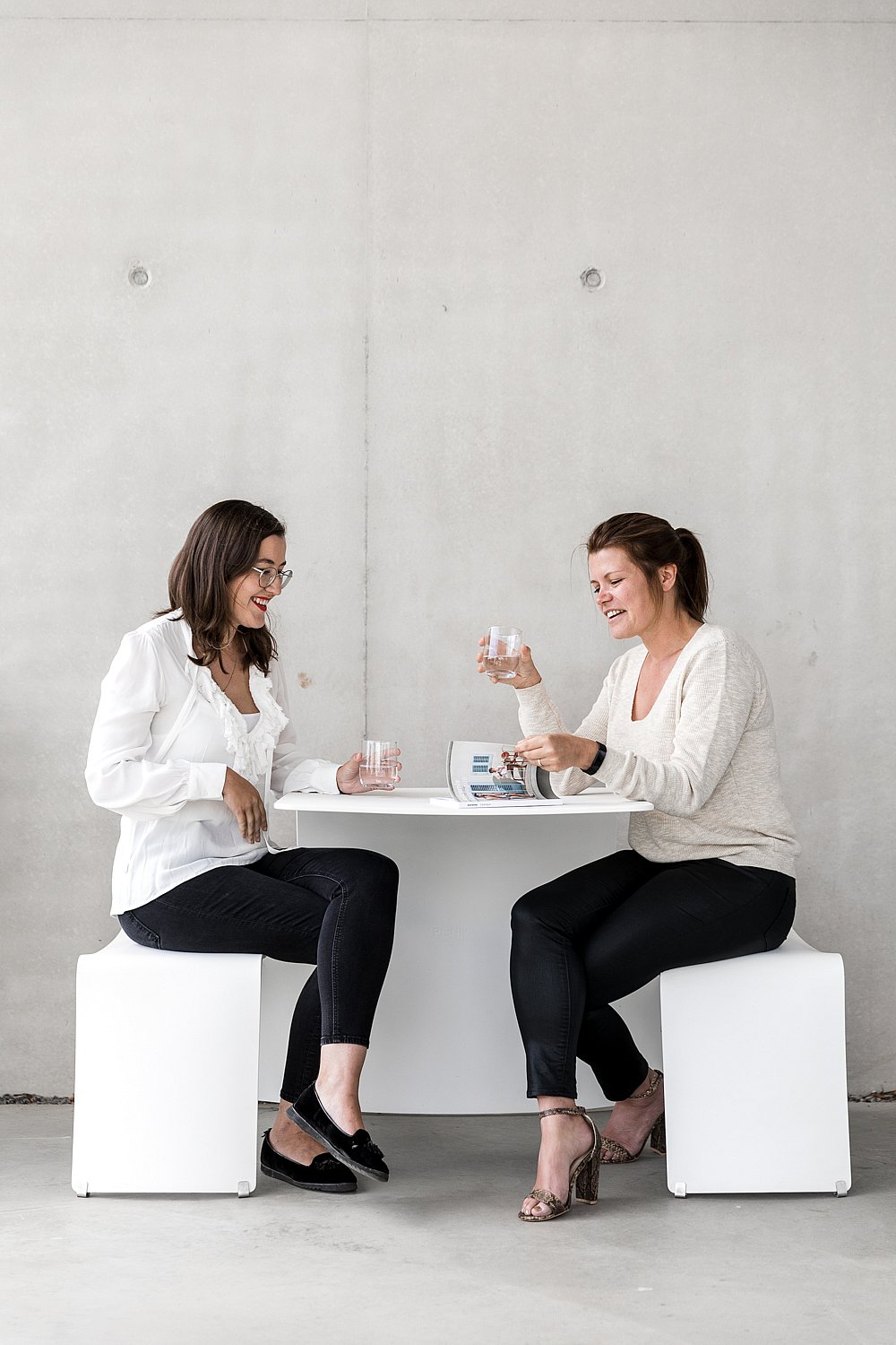 Twee vrouwen zitten samen aan een kleine witte picnikentafel en kletsen over een bril water.