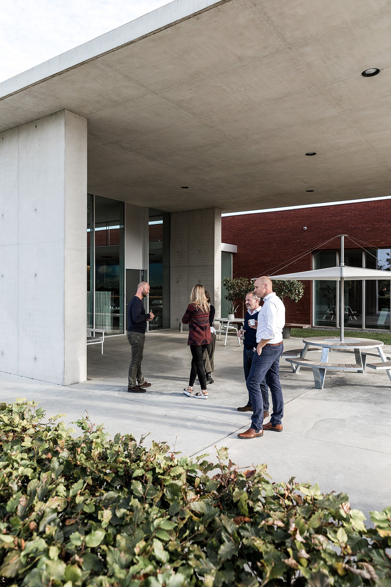 Kleine groep collega's praat buiten bij de ingang van het Extremis-gebouw, met tuinmeubilair op het terras.