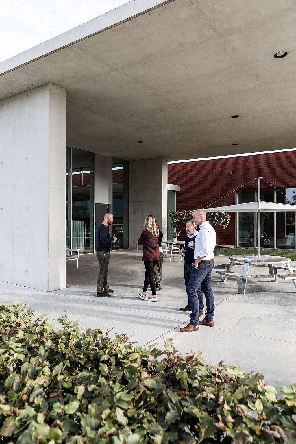Kleine groep collega's praat buiten bij de ingang van het Extremis-gebouw, met tuinmeubilair op het terras.