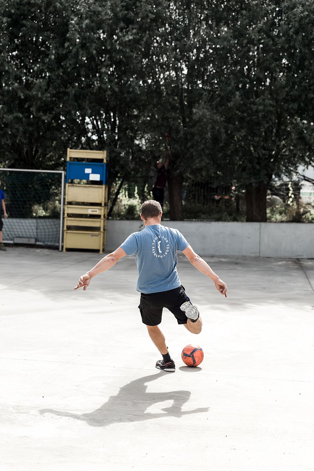 Werknemer van achteren gezien op een buitensportveld, armen wijd verspreid tijdens een speels pauzemoment.