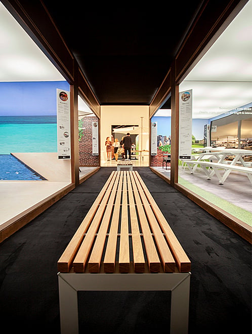 Long banc à lattes en bois exposé dans un couloir d’exposition de style musée, avec des scènes de produits Extremis thématiques visibles des deux côtés.