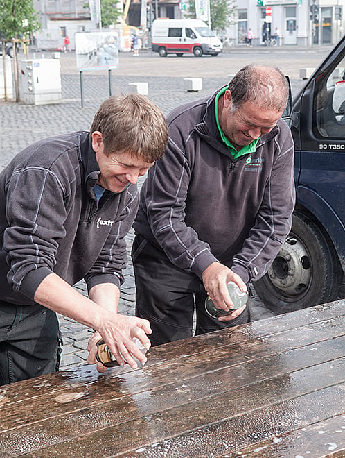 Table de pique-nique Hopper en bois patinée debout à l’extérieur sur une place du marché à Poperinge, montrée avant son nettoyage de printemps.