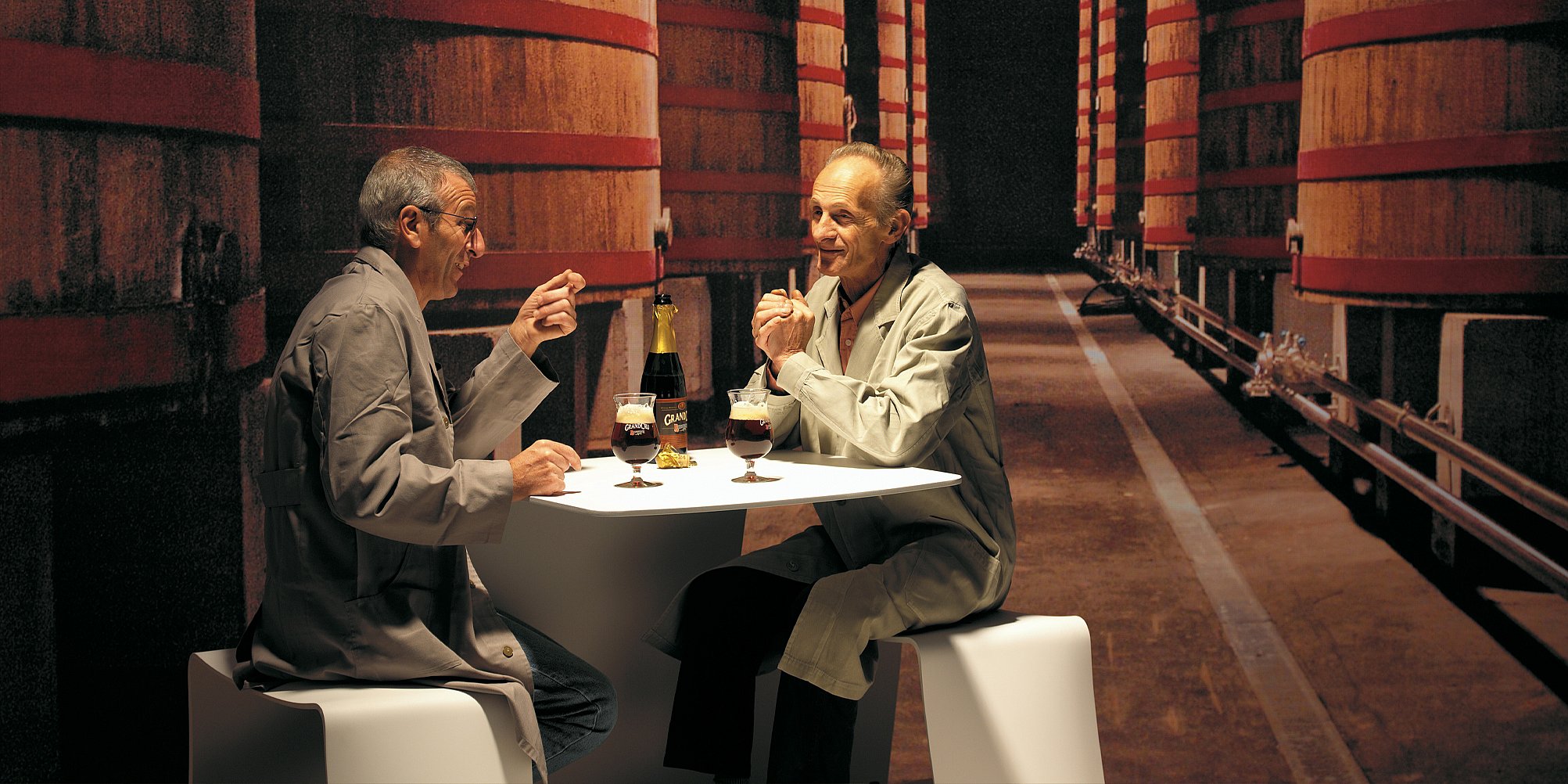 Two people drinking a beer on the picnik table inside a brewery.