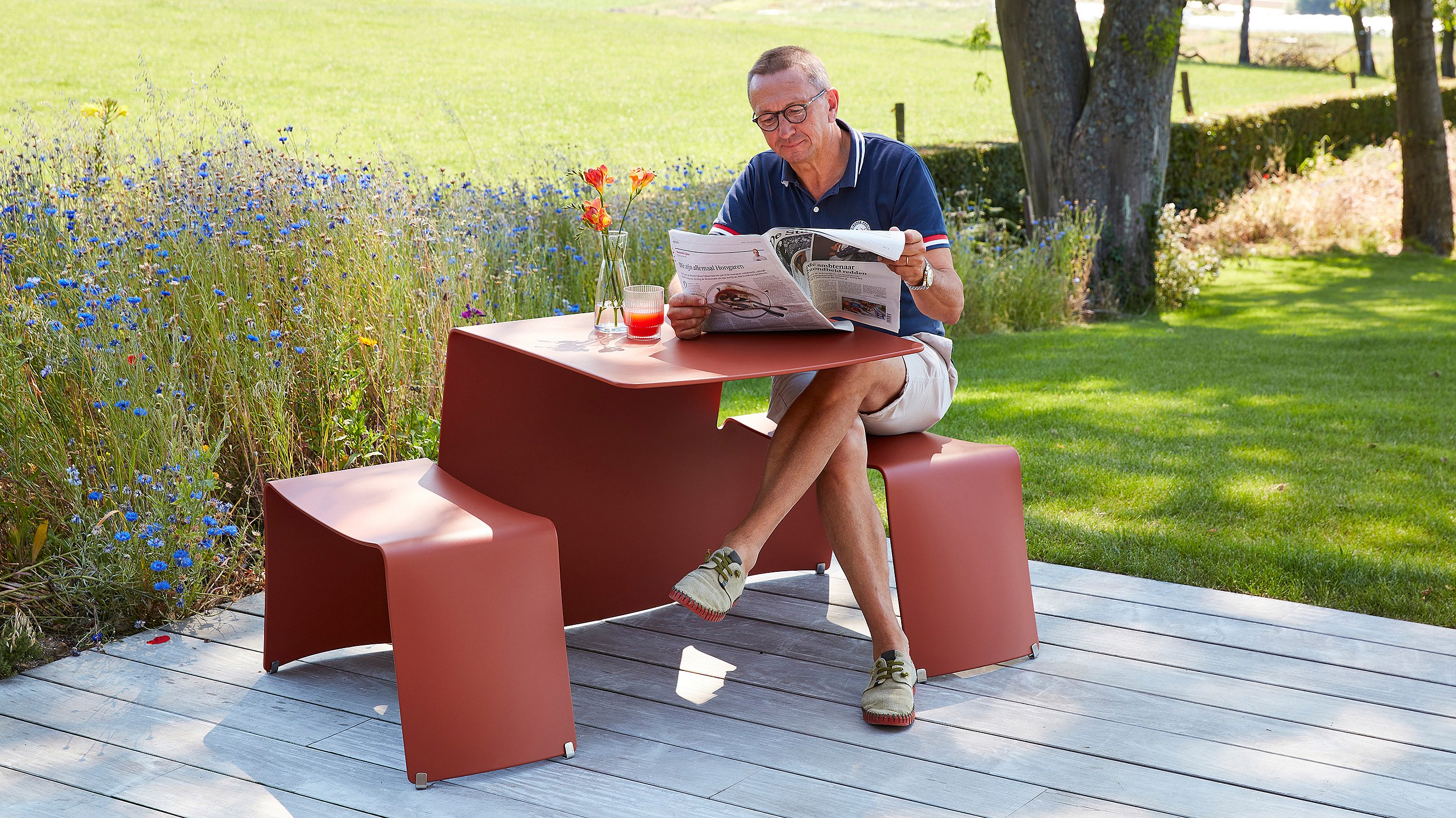 Picnik shown in a real-life reference setting, used as a compact outdoor table for two in a garden or terrace environment.