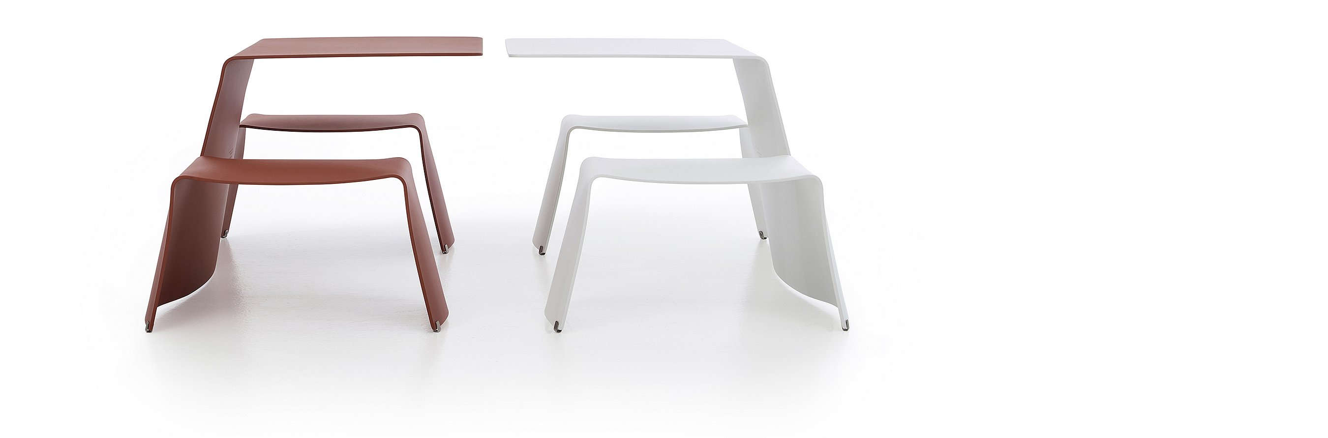 Studio shot of two picnik tables side by side, the left one being red, the right one white.