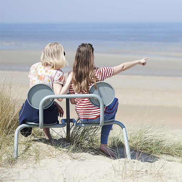 Des femmes assises sur le bistroo dans les dunes pointant vers l’horizon.