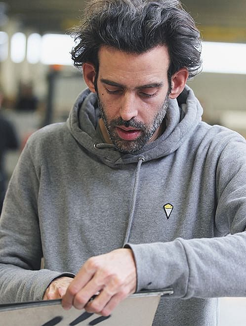 Denis Meyers est assis à une simple table de Picnik rouge sur une palette en bois dans un atelier, peignant à la main des lettres noires sur le plateau.