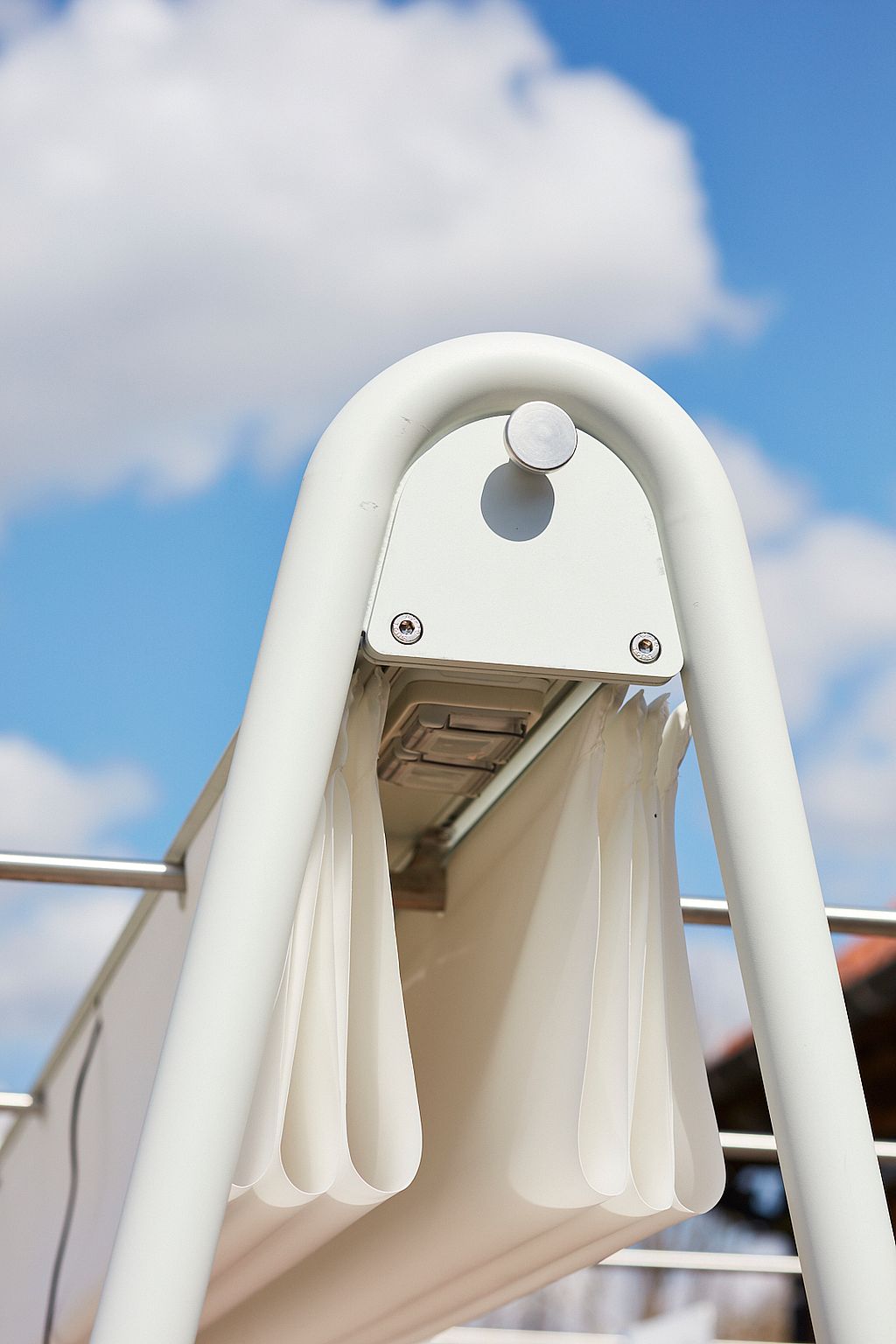 Close-up of the top of the AMAi A-frame with folded shade fabric, metal rails, and integrated components against a blue sky.