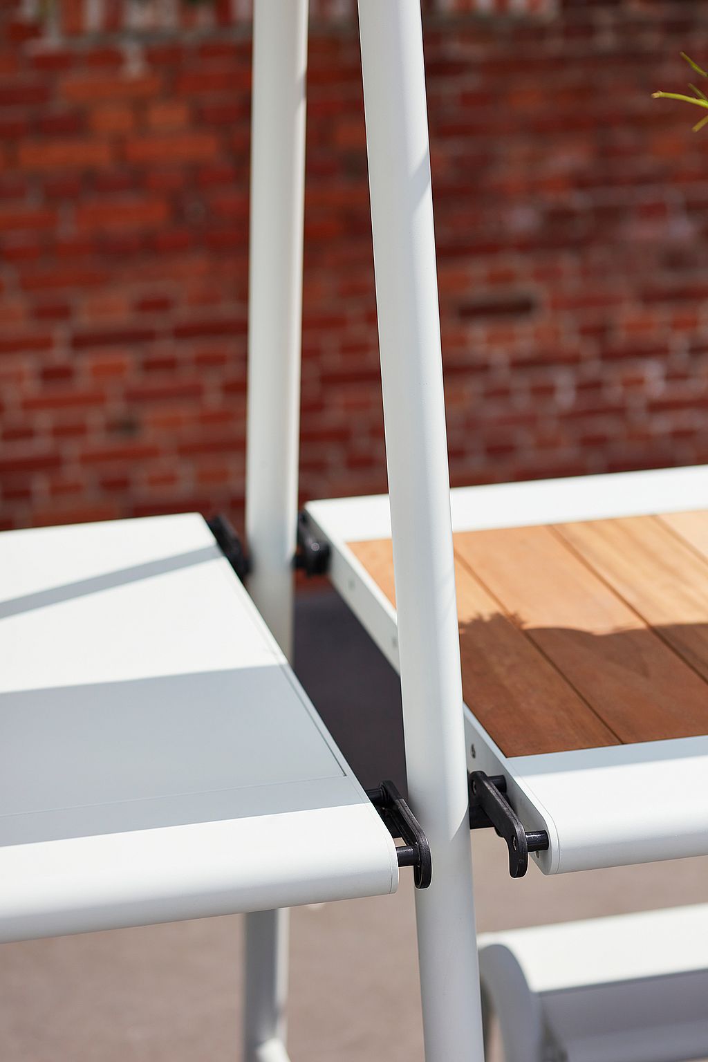 Close-up of two AMAi tabletops attached to the central A-frame, showing black locking brackets and the contrast between white and wooden surfaces.