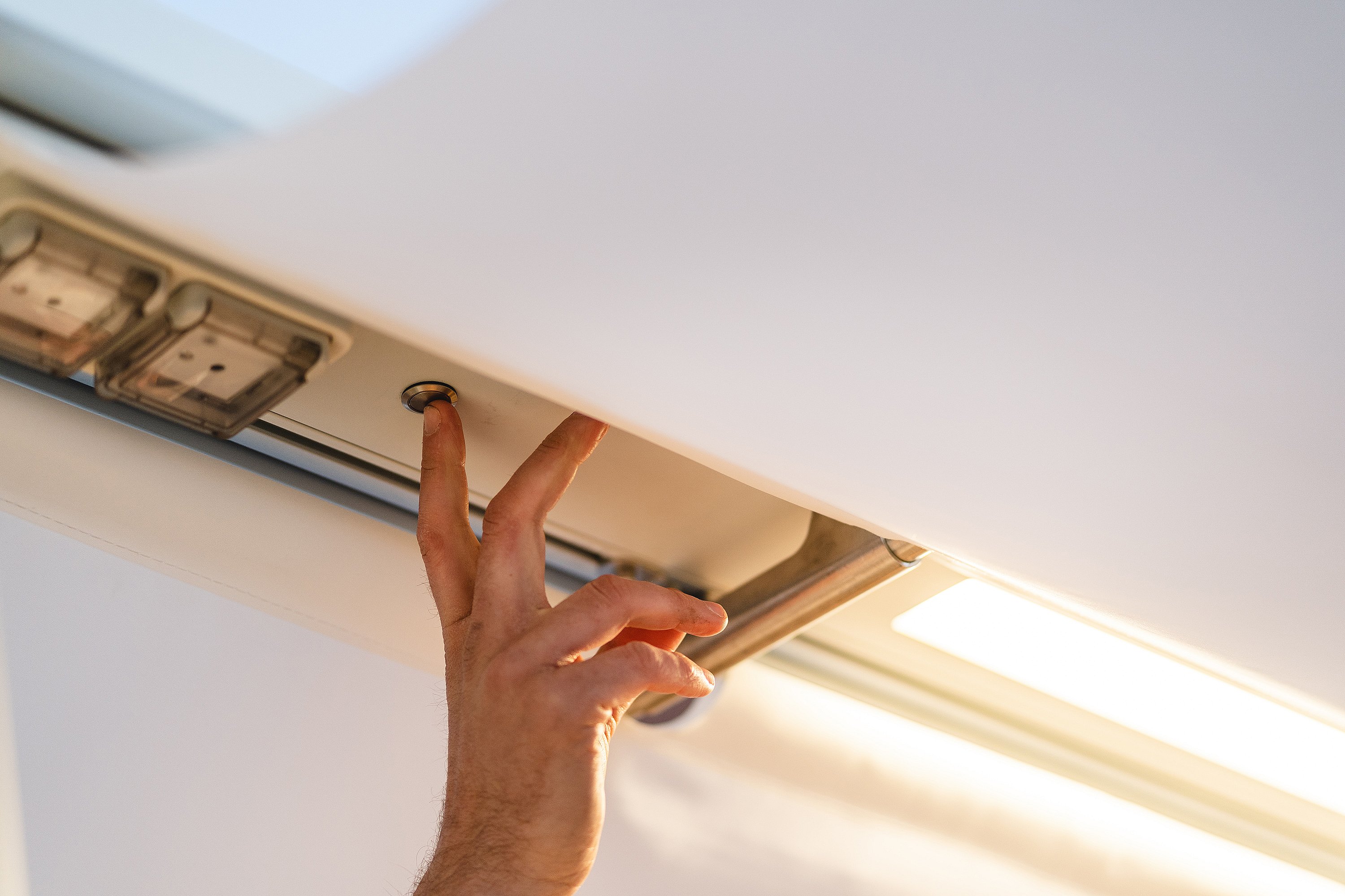 Close-up of a hand pressing a button beneath the AMAi overhead beam, next to integrated lighting and power components.