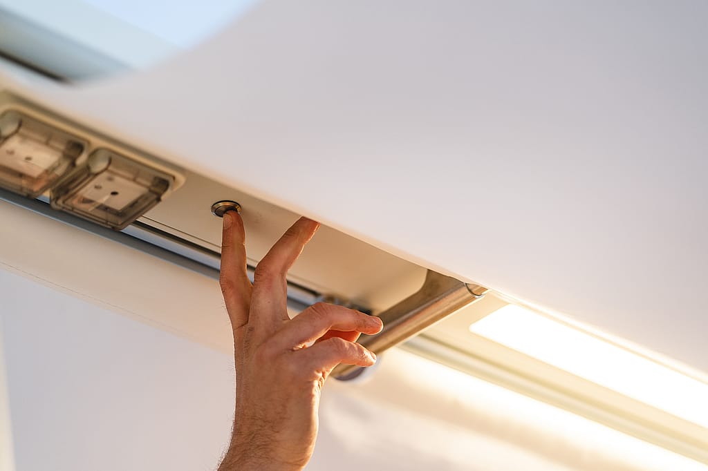 Close-up of a hand pressing a button beneath the AMAi overhead beam, next to integrated lighting and power components.
