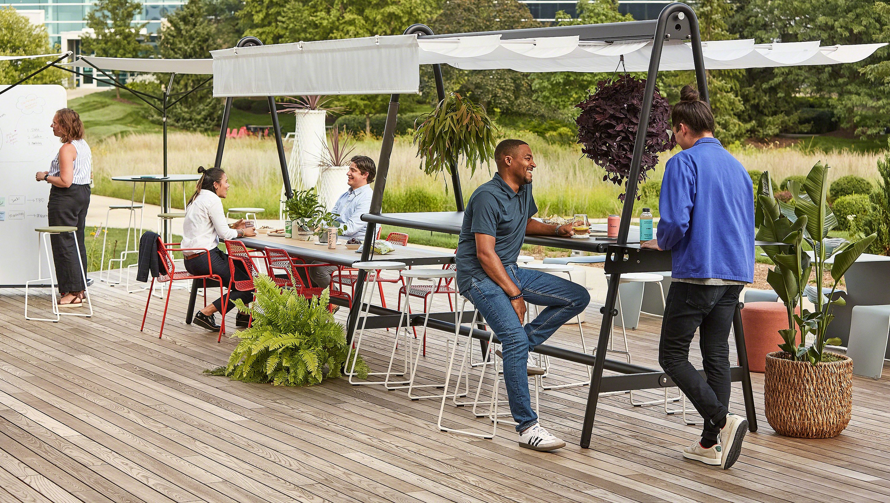 People using an AMAi outdoor workspace with shade in a planted garden setting.