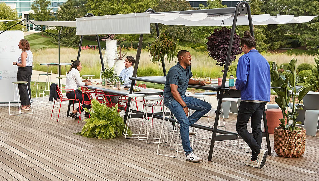 People using an AMAi outdoor workspace with shade in a planted garden setting.