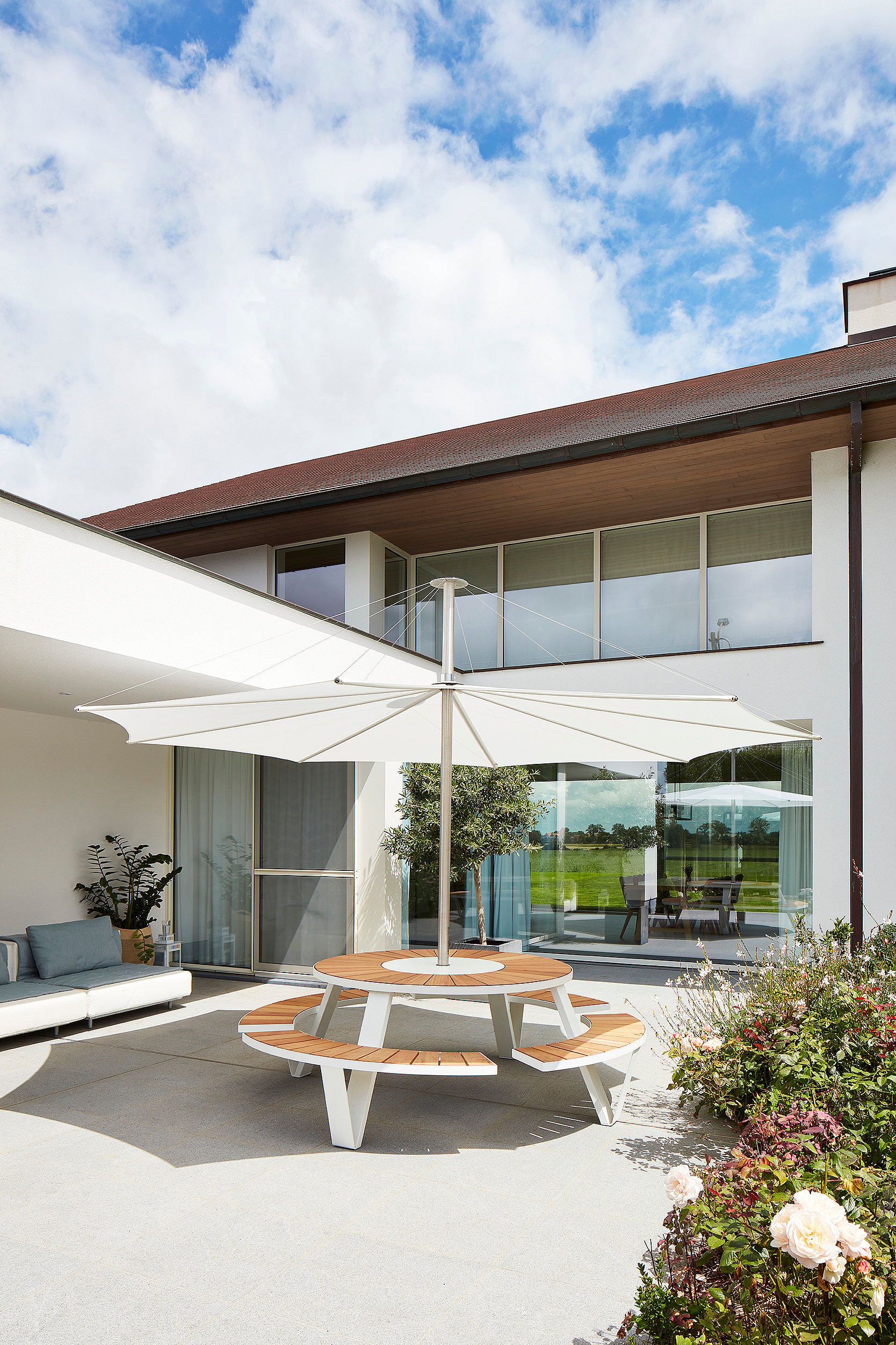Table de pique-nique ronde Pantagruel avec bancs en bois et structure blanche, sous un grand parasol sur une terrasse