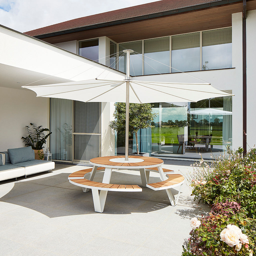 Ronde picknicktafel van Pantagruel met houten zitjes en wit frame onder een grote parasol op een terras