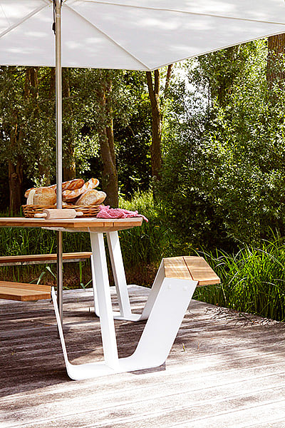 Ankertisch mit Holztischplatte und weißem Rahmen unter einem Inumbrina-Schatten neben hohen Gartengräsern
