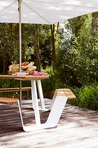 Ankertisch mit Holztischplatte und weißem Rahmen unter einem Inumbrina-Schatten neben hohen Gartengräsern