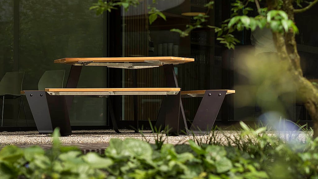Ankertafel met houten banken en zwart frame omgeven door groen op de binnenplaats van de brouwerij
