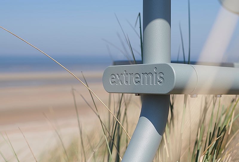 Close-up of the Extremis logo on the verdigris Bistroo frame with beach grass and sea in the background