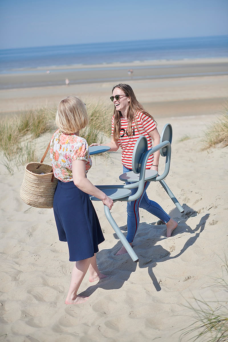 Two women carrying a verdigris Bistroo two-seater across the sand near the beach