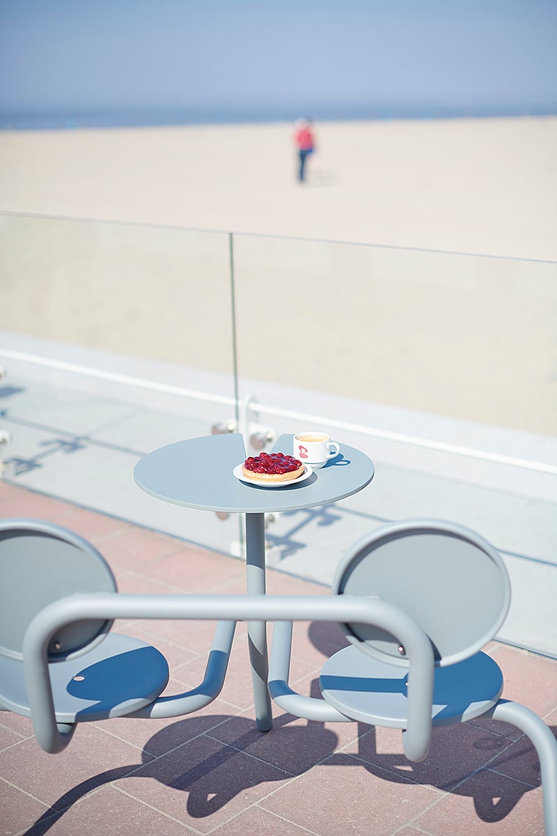 Verdigris Bistroo two-seater in beach grass with a bowl of strawberries and a drink on the tabletop