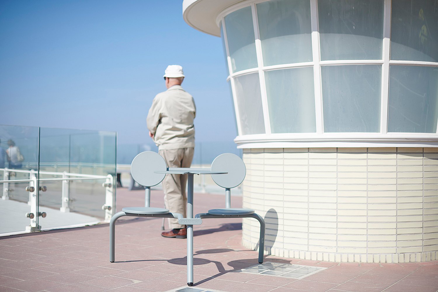 Verdigris Bistroo table and two seats on a seaside terrace beside a curved white building