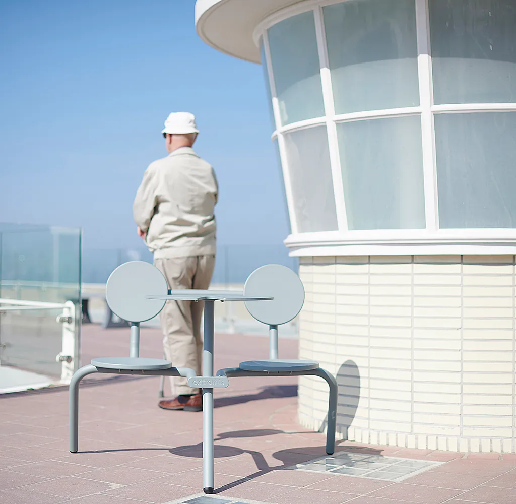 Verdigris Bistroo table and two seats on a seaside terrace beside a curved white building