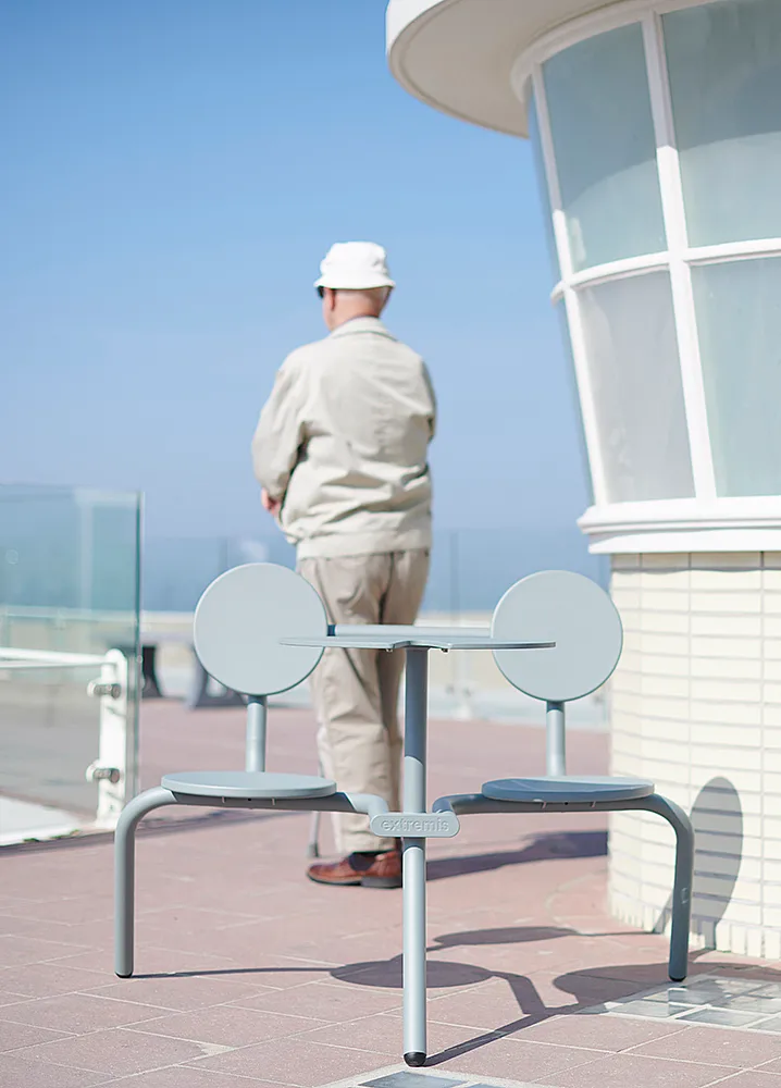 Verdigris Bistroo table and two seats on a seaside terrace beside a curved white building