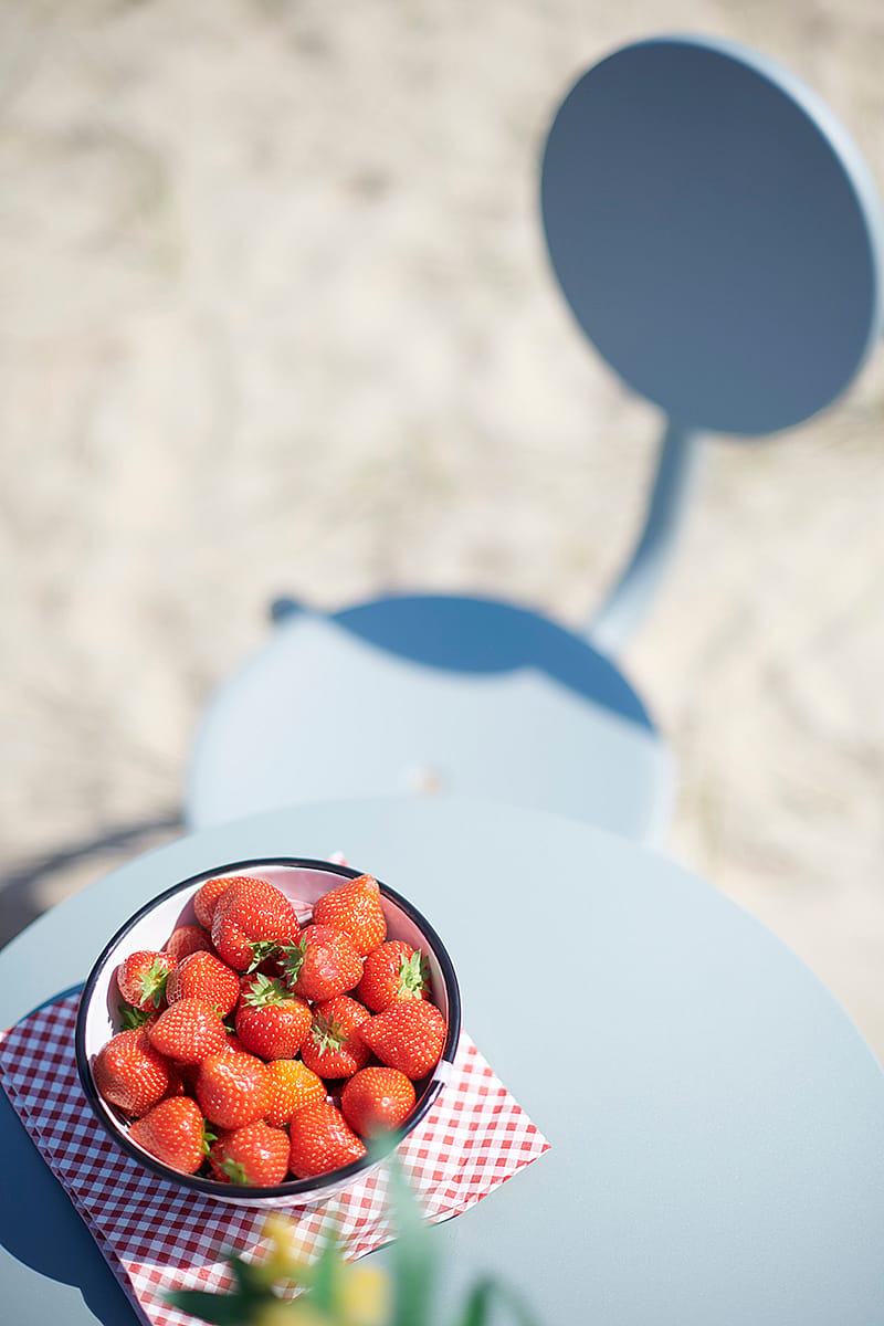Bowl of fresh strawberries on a verdigris Bistroo tabletop with a seat in the background