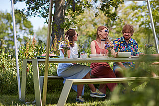 Menschen lächeln um einen Hopper-Picknicktisch mit Picknickessen und Blumen im Schatten